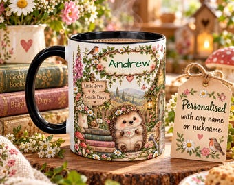 May include: A white ceramic mug with a black handle and rim, featuring a colorful illustration of a hedgehog holding a teacup, surrounded by flowers, books, and the text Andrew, Little Joys & Gentle Days, and a gift tag reading Personalized with any name or nickname.