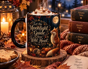 May include: A black ceramic mug filled with whipped cream, featuring a fox, a hedgehog, pumpkins, and autumn leaves. The text reads Let the Moonlight Guide Your Wild Heart. The mug sits on a wooden coaster surrounded by fall decor.