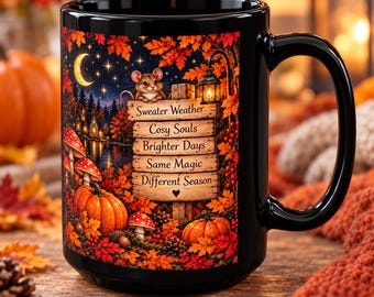 May include: A black ceramic mug featuring a colorful autumn scene with a mouse perched on a wooden sign. The sign displays the text: Sweater Weather, Cosy Souls, Brighter Days, Same Magic, Different Season. The design includes pumpkins, mushrooms, and fall foliage.