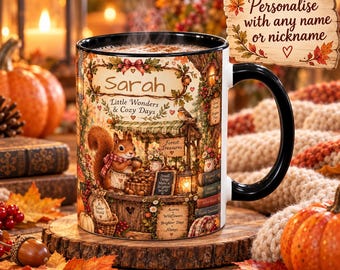 May include: A white ceramic mug with a black handle and rim, featuring a detailed autumn-themed illustration of a squirrel at a market stall, the name Sarah, and the text Little Wonders & Cozy Days, Forest Treasures, and A Kinder World.