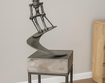 May include: A metal sculpture of a figure snowboarding. The figure is constructed from nuts, bolts, and other metal hardware. The sculpture is mounted on a square metal base with a black metal frame. The snowboarder is angled as if in motion.