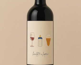 May include: A dark wine bottle with a cream-colored label featuring illustrations of a wine glass, baby bottle, and beer glass. The label also includes the text "bientôt à l'apéro!"