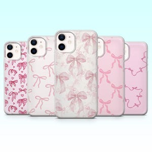 Puede incluir: Colección de cinco fundas para teléfono con varios diseños de lazo rosa. Las fundas presentan diferentes patrones, incluyendo lazos sobre un fondo blanco, una textura similar al mármol y un patrón de lazos repetidos. Las fundas se muestran sobre un fondo azul claro.