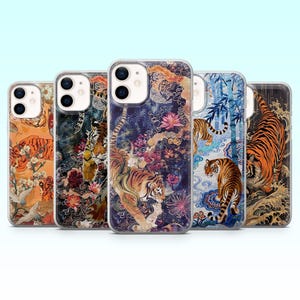 May include: A collection of five phone cases featuring tiger illustrations. Each case showcases a different design with tigers in various poses, set against backgrounds of flowers, waves, and traditional Asian patterns. The cases have a clear, glossy finish.