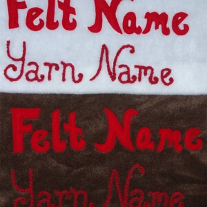 Op de afbeelding: Close-up van twee stofstalen, een wit en een bruin. De woorden "Felt Name" en "Yarn Name" zijn in rood geborduurd op beide stalen.