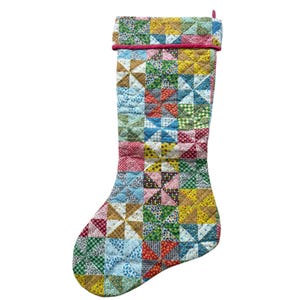 Puede incluir: Un calcetín navideño acolchado con un diseño de patchwork de cuadrados de tela multicolor con varios patrones florales y geométricos. El calcetín tiene un puño doblado en la parte superior con un borde rosa fino y una pequeña trabilla.