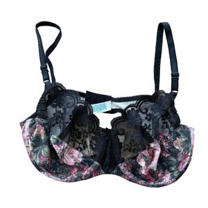May include: Black bra with floral print and lace detailing. The bra features adjustable straps and a scalloped edge. The cups are adorned with a pink, green, and black floral pattern, and the center is made of black lace.