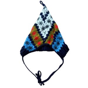 May include: A pointed knit hat featuring a colorful geometric pattern of white, olive green, and light blue diamonds. The design includes black snowflake motifs and bright red star accents. It has dark blue ear flaps and chin ties.