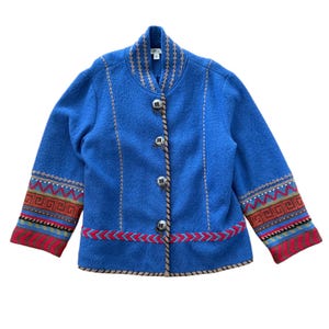 May include: A bright blue jacket featuring a stand-up collar, four silver-toned metal buttons, and decorative embroidery along the front panels. The sleeves and hem are accented with colorful geometric patterns in red, green, and tan.