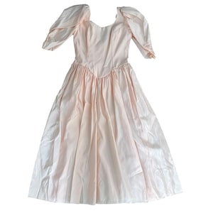 Könnte beinhalten: Ein hellrosa Vintage-Kleid mit einem Rundhalsausschnitt und kurzen, gepufften Ärmeln. Das Kleid hat ein figurbetontes Oberteil und einen vollen, fließenden Rock. Der Stoff hat einen leichten Glanz und das Kleid scheint aus einem leichten Material zu sein.