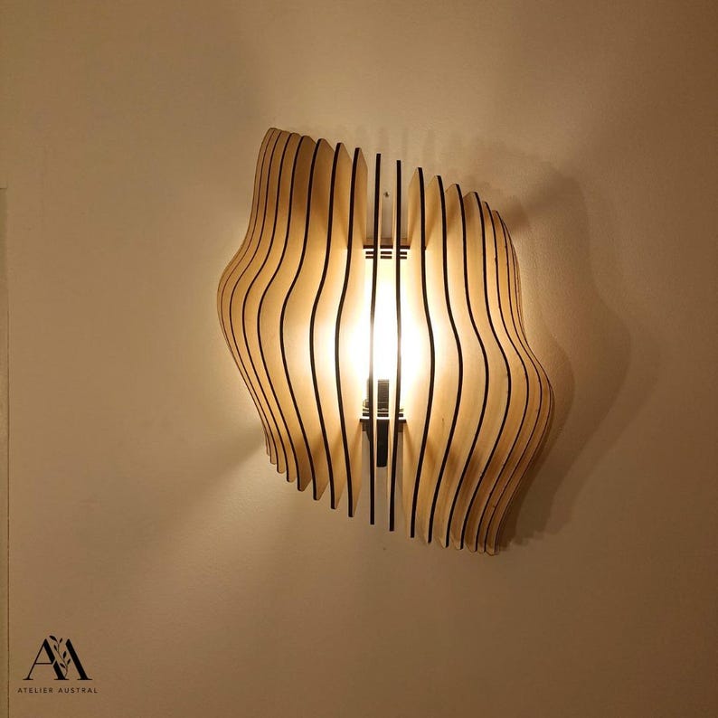 May include: A wooden wall sconce with a unique, wavy design. The light fixture is made of thin, vertical wooden slats with black edges, creating a layered effect. The light shines through the slats, illuminating the room. The sconce is mounted on a wall.