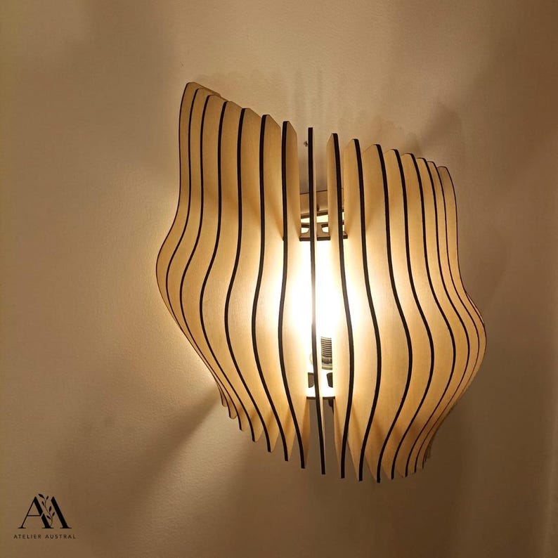 May include: A wooden wall sconce with a unique, wavy design. The light fixture is made of light-colored wood with vertical black lines, creating a layered effect. The light shines through the wooden slats.