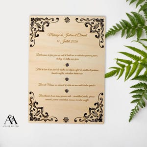 May include: A wooden wedding menu with ornate black corner designs and text in French. The menu includes the names Justine and Climent, the date July 11, 2026, and a list of dishes. The Atelier Austral logo is in the lower left corner.
