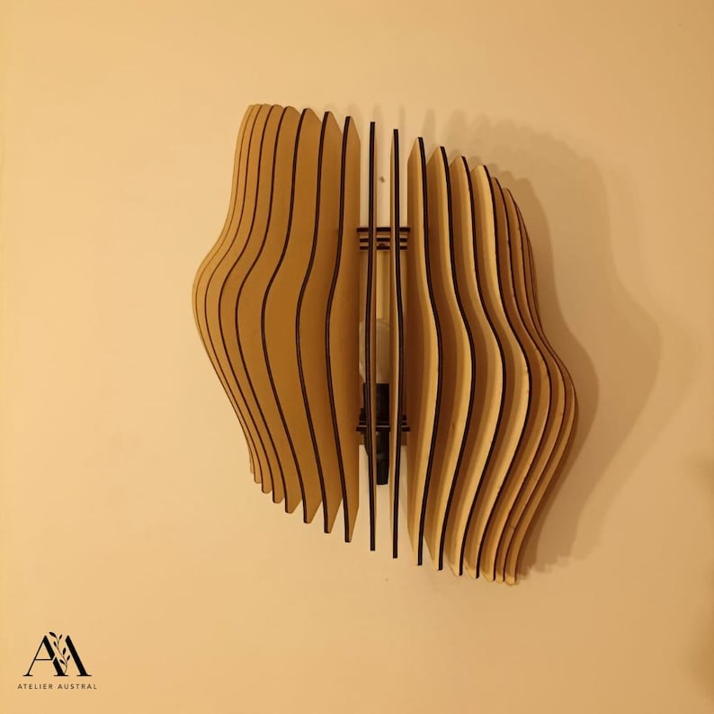 May include: A wooden wall sconce with a unique, layered design. The sconce is made of light-colored wood with dark lines between each layer, creating a wavy, organic shape. The sconce is mounted on a beige wall.