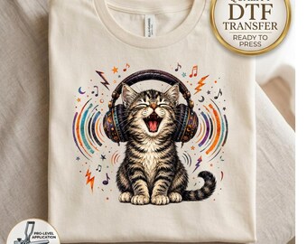 May include: A cream-colored t-shirt featuring a graphic of a tabby kitten wearing large headphones with its mouth open. The design includes colorful sound waves, musical notes, and stars. A gold circular badge reads High Quality DTF Transfer.