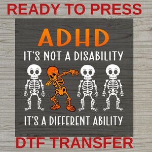 May include: A rectangular transfer sheet featuring the text READY TO PRESS at the top and DTF TRANSFER at the bottom. The center displays the orange text ADHD, followed by IT'S NOT A DISABILITY, three white skeletons, one orange dabbing skeleton, and IT'S A DIFFERENT ABILITY.