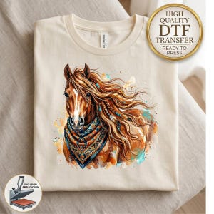 May include: A cream-colored t-shirt featuring a watercolor-style illustration of a brown horse with a flowing mane adorned with beads and feathers. The horse wears a patterned bandana in shades of orange, blue, and black. Text reads HIGH QUALITY DTF TRANSFER.