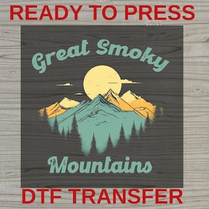 May include: A square DTF transfer sheet featuring a graphic of the Great Smoky Mountains with a large yellow sun, teal mountain peaks, and dark green pine trees. The text reads Great Smoky Mountains in a curved teal font on a dark background.