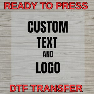 May include: A graphic design featuring the words "READY TO PRESS" and "DTF TRANSFER" in red, with "CUSTOM TEXT AND LOGO" in black. The background has a wood grain texture.