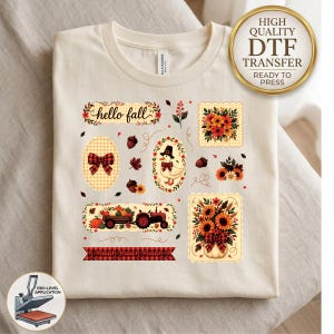 May include: A cream-colored t-shirt featuring a graphic print with the text hello fall, a duck wearing a hat, a red and black buffalo plaid bow, a tractor pulling pumpkins, and various autumn-themed floral arrangements and leaves.