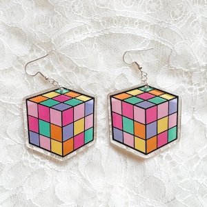 May include: Two hexagonal earrings with a Rubik's Cube design. The cubes are made up of brightly coloured squares in pink, orange, yellow, green, and purple. The earrings have silver-tone ear wires and are a fun, retro accessory.