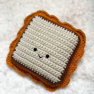 May include: A crocheted sandwich with a smiling face. The sandwich has a white center, brown edges, and a scalloped orange crust. The word "pattern" is at the bottom of the image.