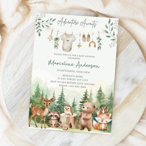 Puede incluir: Invitación a un baby shower con el texto "Adventure Awaits" y detalles para el baby shower de Marceline Anderson. El diseño presenta animales del bosque, una escena forestal e ilustraciones temáticas de bebés.