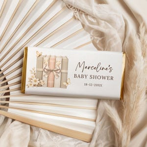 Puede incluir: Envoltorio de barra de chocolate con temática de baby shower. El diseño presenta una pila de libros atados con un lazo, mariposas y adornos florales. El texto dice "Marceline's BABY SHOWER 18-12-20XX."