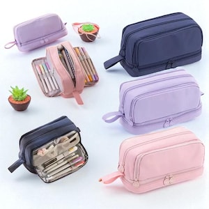 May include: A collection of colorful pencil cases in various shades of pink, purple, and navy blue. Some cases are open, revealing pens, pencils, and other stationery items. Each case has a zipper closure and a small handle.