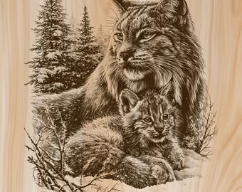 May include: A dark brown laser-engraved illustration on a light wood surface depicting an adult lynx and a lynx kitten resting together. The scene includes detailed fur textures, pointed ears, and a background of snow-covered pine trees and branches.