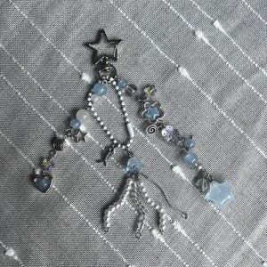 May include: A silver keychain with multiple charms. The charms include a star, hearts, and blue and white beads. The keychain is on a gray striped background.
