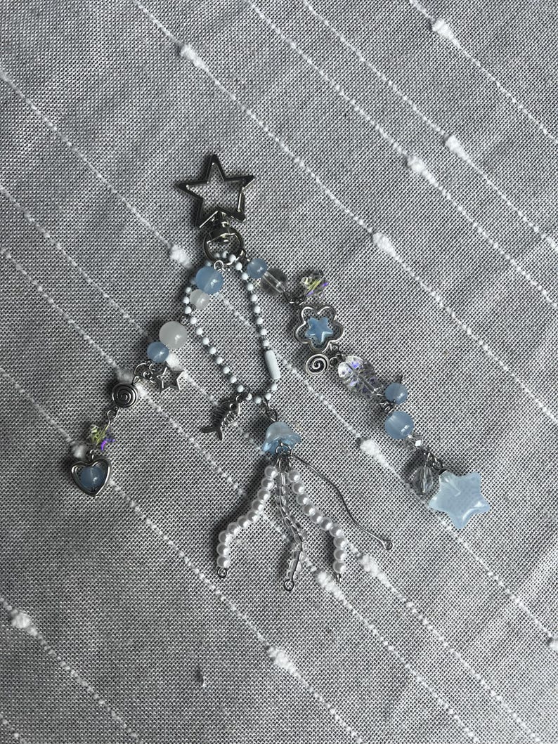 May include: A silver keychain with multiple charms. The charms include a star, hearts, and blue and white beads. The keychain is on a gray striped background.