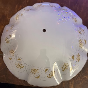 May include: A white, scalloped-edge ceiling light fixture with a gold floral pattern. The fixture has a single central hole and is made of a translucent material. The gold design is a repeating pattern around the edge.