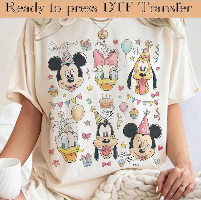 K&ouml;nnte beinhalten: Cremefarbenes T-Shirt mit den Zeichentrickfiguren Mickey Mouse, Daisy Duck, Pluto, Donald Duck, Goofy und Minnie Mouse. Das Design umfasst Partyh&uuml;te, Luftballons, Cupcakes und den Text "Ready to press DTF Transfer".