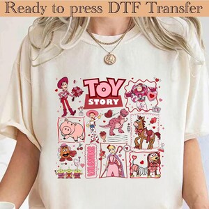 Puede incluir: Camiseta color crema con un gr&aacute;fico colorido de "Toy Story" con varios personajes y el texto "Toy Story". Las palabras "Ready to press DTF Transfer" est&aacute;n en la parte superior.