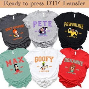 Puede incluir: Seis camisetas con personajes de "A Goofy Movie". Cada camiseta muestra el nombre de un personaje en negrita, junto con el texto "EST. 1995 A GOOFY MOVIE". Los colores incluyen gris, blanco, negro, rojo y verde azulado.