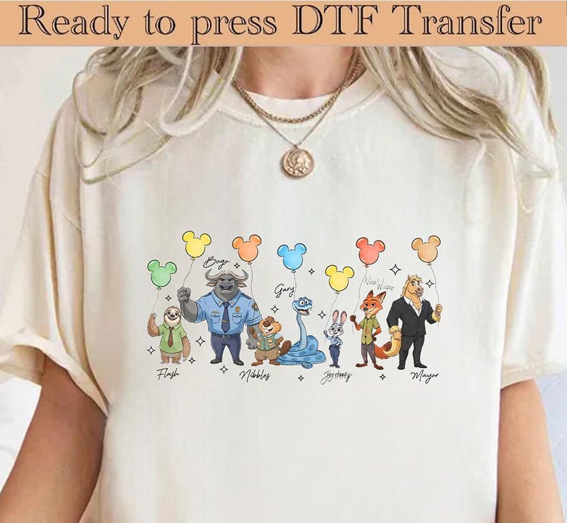 May include: Cream-colored t-shirt featuring a DTF transfer of Zootopia characters holding Mickey Mouse-shaped balloons. The characters include Flash, Bogo, Nibbles, Gary, Judy Hopps, Nick Wilde, and Mayor Lionheart. Text at the top reads "Ready to press DTF Transfer."