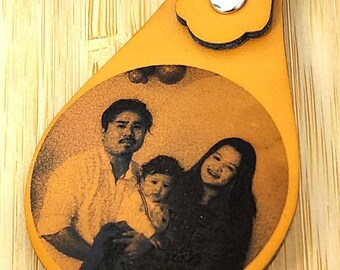 May include: A car key fob and a leather keychain with a family photo. The keychain is a light orange color and has a metal ring and clasp. The key fob is black.