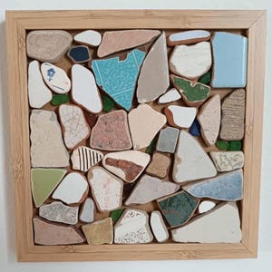 Può includere: Opera d'arte a mosaico quadrata con cornice in legno. Il mosaico è composto da vari frammenti ceramici di forma irregolare nei toni del beige, blu, verde e rosa. Alcuni pezzi hanno motivi.