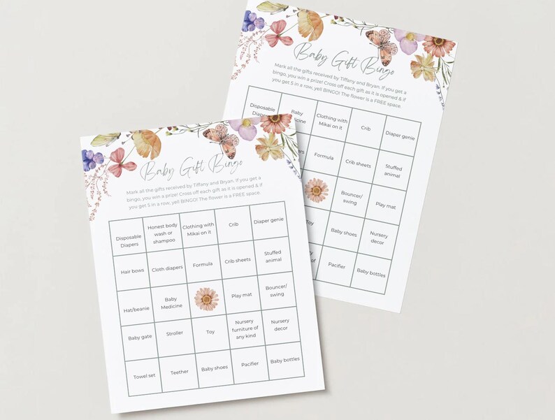May include: Two baby gift bingo cards with floral and butterfly illustrations. The cards have a grid layout with various baby-related terms. The text "Baby Gift Bingo" is at the top, with instructions below.