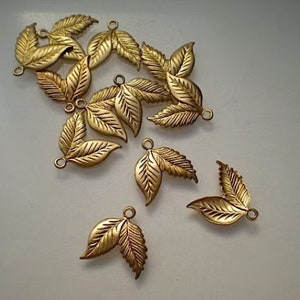 Puede incluir: Un grupo de 12 abalorios de hoja de metal dorado con una superficie texturizada. Los abalorios tienen un bucle en la parte superior para sujetarlos a joyas u otras manualidades.
