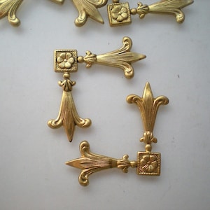 May include: A set of eight gold-toned metal decorative corner pieces. Each piece features a stylised floral design with a small square in the centre.