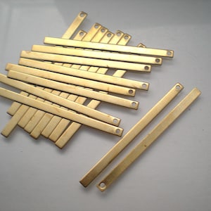 May include: A group of 14 gold-colored metal strips with rounded ends and two small holes in each strip. The strips are arranged in a fan shape, with the longest strip at the bottom and the shortest strip at the top.