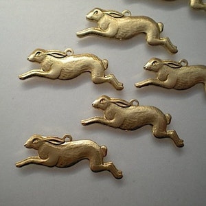 Puede incluir: Cinco dijes de metal de color dorado, cada uno representa un liebre en una pose de carrera. Los dijes son detallados y tienen un acabado texturizado.