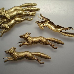 May include: Five gold-colored metal fox figurines. The foxes are in various poses, some are leaping, some are running, and some are standing. The figurines are detailed and have a realistic appearance.