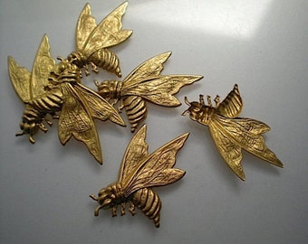 May include: Four gold-colored metal bee figurines with detailed wings and bodies. The bees are arranged in a cluster on a white surface.