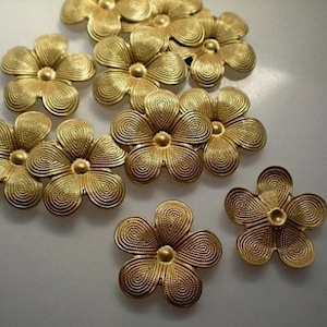 May include: A collection of ten gold-colored metal flower embellishments. Each flower has five petals with a textured, swirling design. The flowers are approximately 1 inch in diameter.
