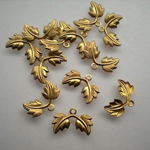 May include: A set of 14 gold-toned metal leaf-shaped charms with a loop at the top. The charms are arranged in a random pattern on a white surface.
