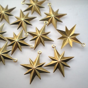 Puede incluir: Una colección de doce abalorios de metal de color dorado en forma de estrella con una punta puntiaguda y un bucle en la parte superior.