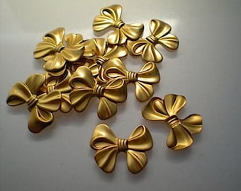 May include: A collection of gold-colored bow-shaped embellishments. The bows have a textured, metallic appearance and are arranged in a scattered pattern. The bows are likely decorative elements for crafts or accessories.